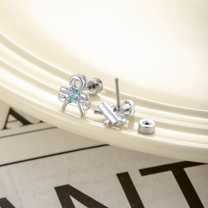 Silver bow stud earring with light blue zircon and screw back on a ceramic plate