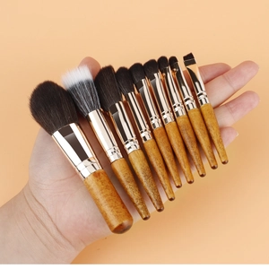 Detailed view of nine mini makeup brushes with wooden handles held in hand for size