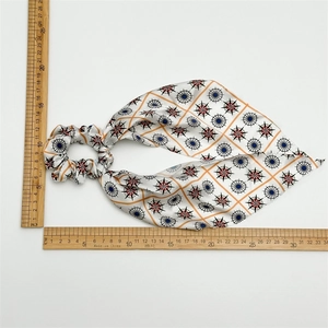 Detail of silk-feel bow hair scrunchie with red and blue star patterns and ruler measurement
