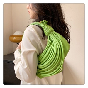 Sac à bandoulière en cuir tressé vert vif porté par un mannequin dans un intérieur chic
