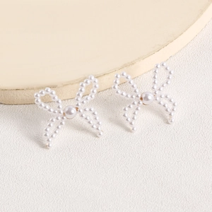 Detailed close-up of handmade white pearl bow earrings with elegant golden metal base