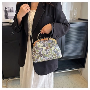 Detail of floral shell bag featuring a metal frame clasp and elegant gold chain strap