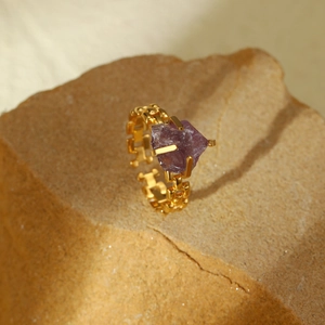 Adjustable gold chain ring with raw purple natural stone on a textured rock surface