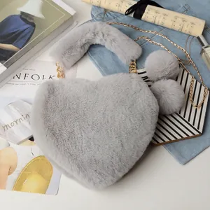 Detail of gray heart-shaped faux fur bag with golden chain and soft pompom charms