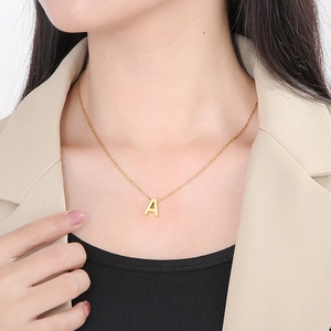 Detail of a minimalist gold A-letter pendant necklace worn on a model neckline