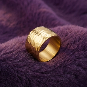 Detailed macro view of wide golden stainless steel ring with hammered texture on plush fabric