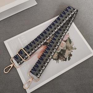 Detail of adjustable woven wide shoulder strap with blue checkered pattern and gold hardware