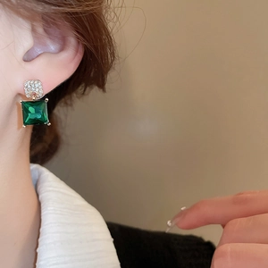 Close-up of square green crystal earrings with diamond accents on model ear