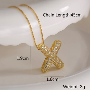 Detail view of a gold X-letter pendant necklace with zircon on a ceramic plate