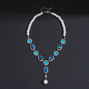 Macro detail of vintage necklace featuring blue gems and pearl drop on black background