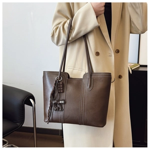 Detail of deep brown tote bag with white contrast stitching and a black cat charm