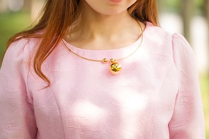 Gros plan d'un collier ras du cou en acier doré avec pendentif boule creuse sur un mannequin