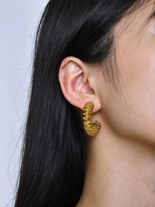 Detailed close-up of gold C-shaped twisted metal wire earrings on model ear