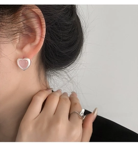 Close-up of pink heart stud earrings and minimalist silver ring on model