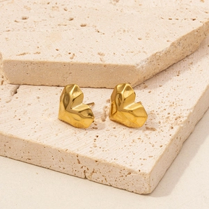 Macro shot of gold heart stud earrings with faceted geometric surface on beige stone