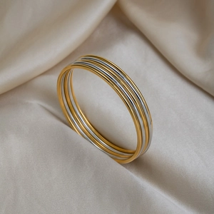 Close-up of minimalist gold and silver bangles stacked on elegant champagne satin fabric
