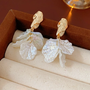 Macro shot of gold metal earrings with iridescent white shell petals on velvet display