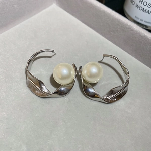 Orecchini a cerchio ritorti color argento con grandi perle color crema su velluto grigio.