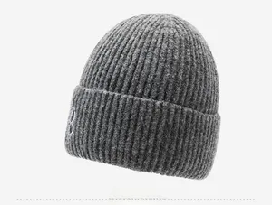 Détail du bonnet en maille grise montrant la texture épaisse et la broderie B blanche