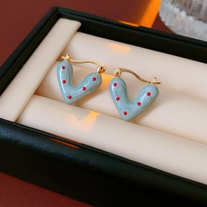 Macro shot of V-shaped gold earrings with red polka dots and blue-grey enamel finish