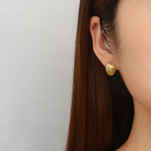 Detailed close-up of golden shell textured geometric C-shaped stainless steel earrings on ear