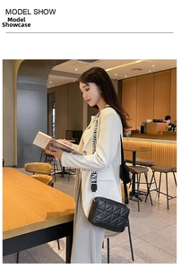Gros plan du sac à bandoulière matelassé noir avec large sangle lettrée au café