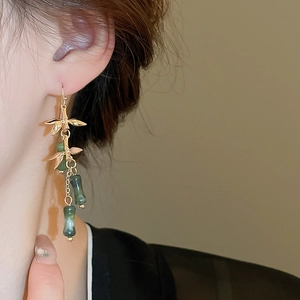 Detail of bamboo joint earrings with green jade beads and golden tassels worn by model