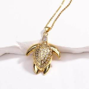 Macro shot of gold turtle pendant with sparkling cubic zirconia on white stone background