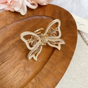 Close-up of golden hollow butterfly hair claw with white pearls on a wooden tray