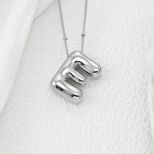 Close-up of a silver balloon style letter E pendant on a delicate bead chain necklace