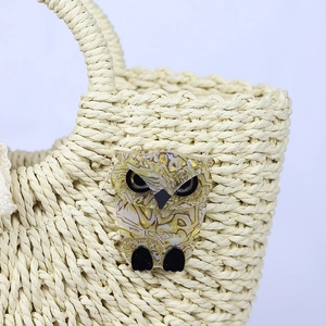 Straw handbag with resin owl charm detail on beige woven texture surface