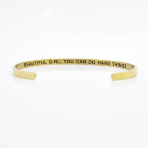 Macro view of golden stainless steel cuff with engraved motivational quote on inner band