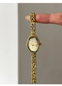 Gros plan sur la montre vintage dorée avec cadran ovale et bracelet tressé orné