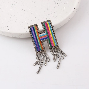 Macro detail of H-shaped brooch with colorful beadwork and dangling rhinestone tassels