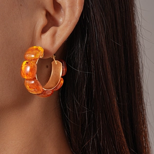 Close-up of a model wearing amber resin C-shaped hoop earrings with a retro glossy finish