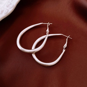 Detail of silver drop-shaped hoop earrings with a matte brushed finish on brown satin