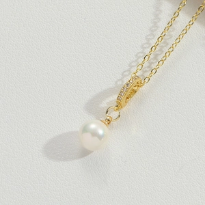 Detail of elegant gold necklace featuring a round pearl pendant with zircon inlay