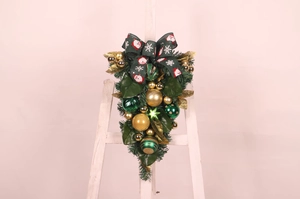 Detailed view of Christmas door hanging with green ribbons, gold ornaments and pine needles