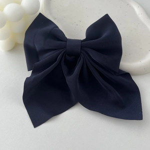 Close-up of a large vintage navy blue fabric bow hair clip on a white ceramic tray