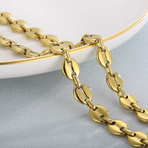 Golden stainless steel coffee bean link necklace on a ceramic plate, elegant jewelry style