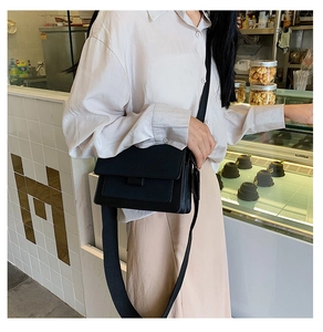 Detail of a minimalist black crossbody flap bag featuring a matte finish and wide strap