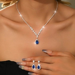 Detailed view of silver necklace and earrings set with pear-shaped blue zircons on model