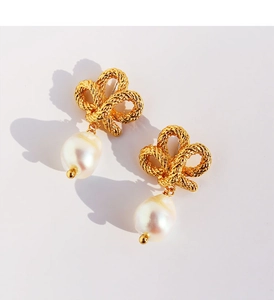 Detail of twisted gold bow earrings with elegant white drop pearls on a beige surface