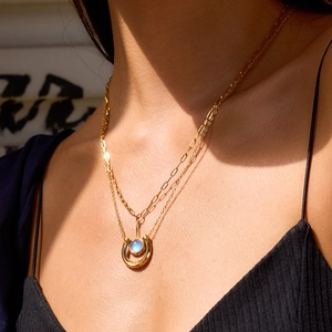 Double layered gold necklace with horseshoe pendant and round blue gemstone on model
