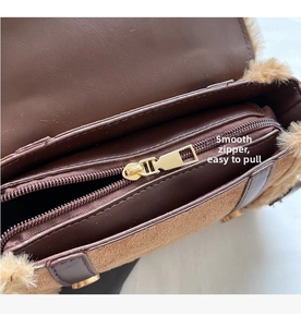 Detail of smooth gold zipper and faux shearling trim on brown leather crossbody bag