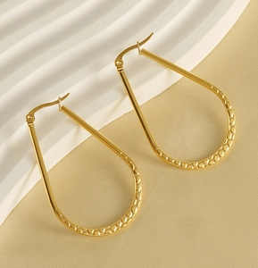 Détail de grandes boucles d'oreilles dorées en goutte avec motif alvéolé texturé