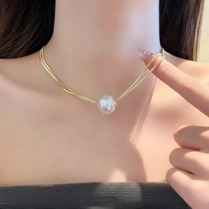 Double-layered gold snake chain necklace with central white pearl shown on model neck
