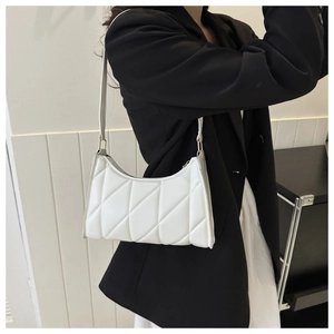 Detail view of white quilted baguette bag with diamond pattern on model shoulder