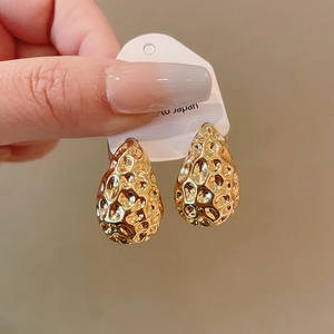Detailed view of gold teardrop earrings with hammered texture on a display card