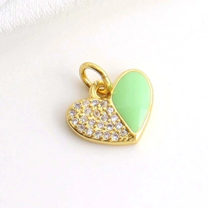 Macro shot of gold heart pendant with green enamel and small diamonds on white silk